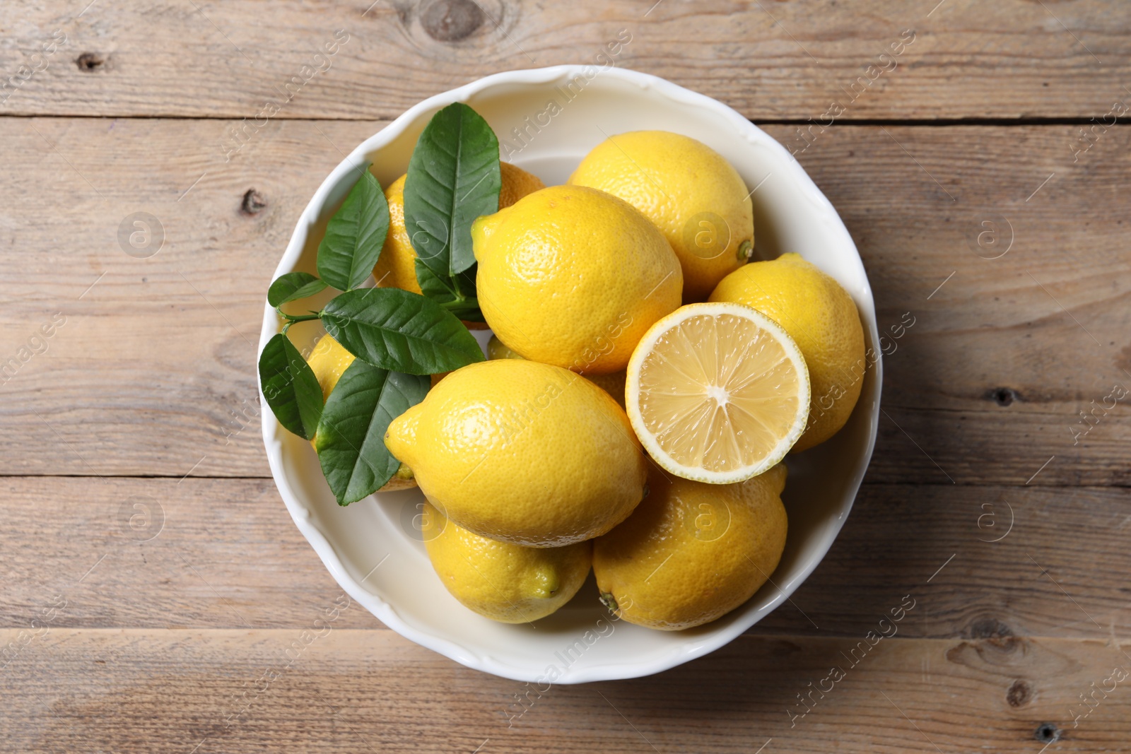 Photo of Fresh lemons and green leaves on wooden table, top view