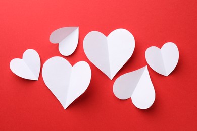 White paper hearts on red background, flat lay