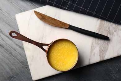 Stone board with saucepan of clarified butter and knife on table, flat lay