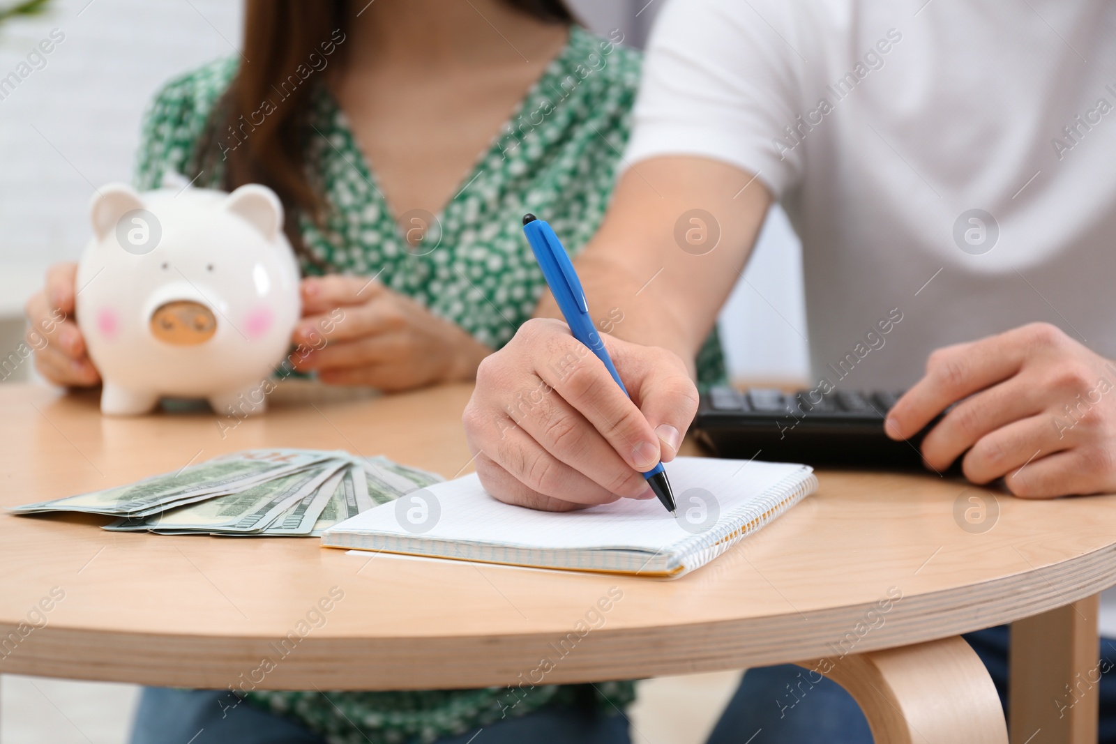 Photo of Young couple with piggy bank and money at table, closeup