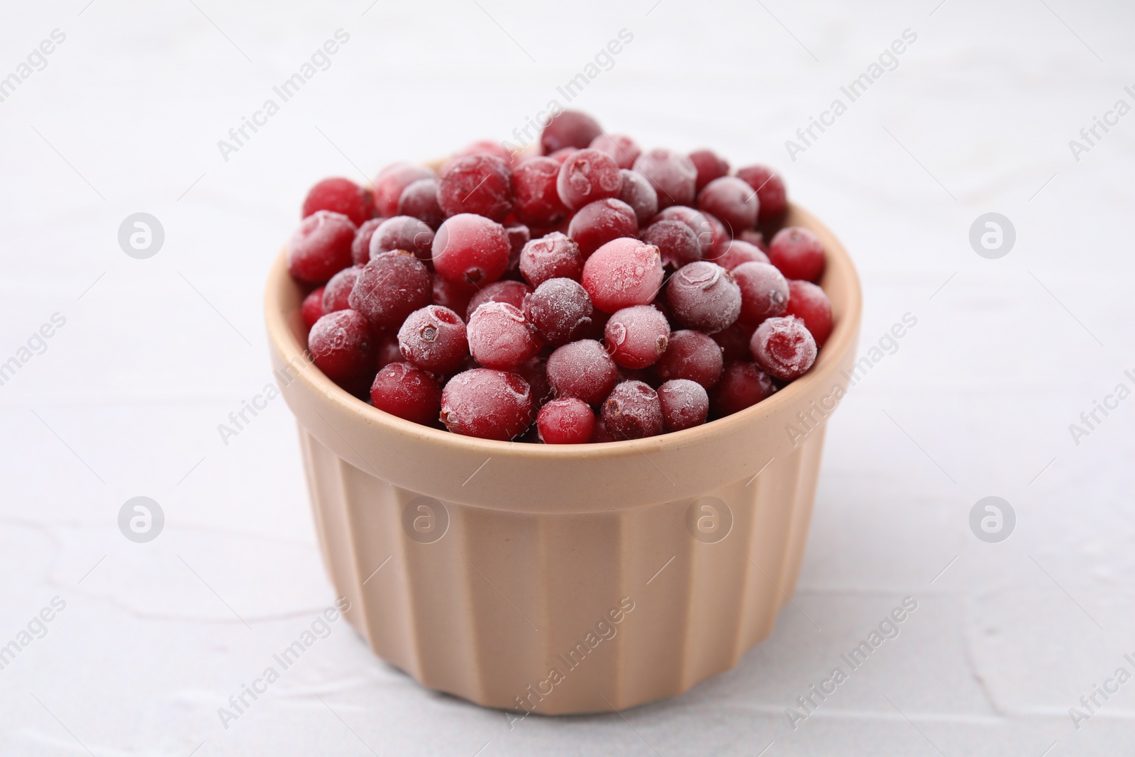 Photo of Frozen red cranberries in bowl on white table, closeup