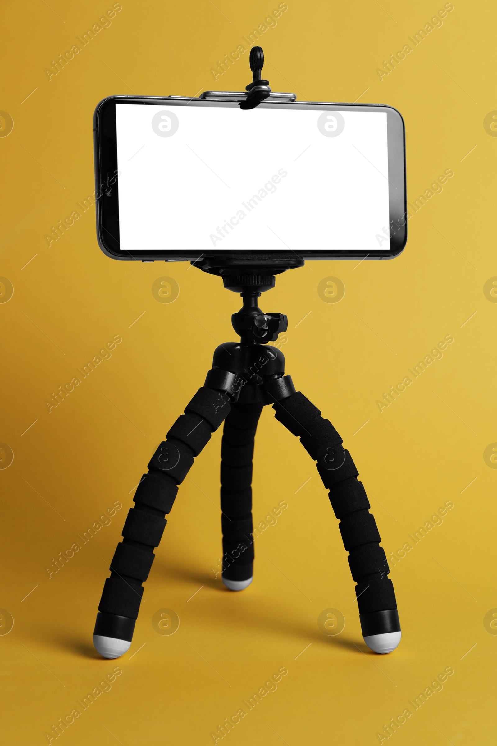 Photo of Modern tripod with smartphone on yellow background
