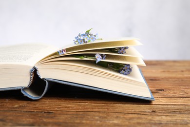 Photo of Beautiful forget-me-not flowers and book on wooden table against light background, closeup