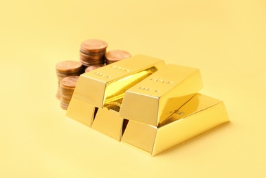 Shiny gold bars and coins on color background