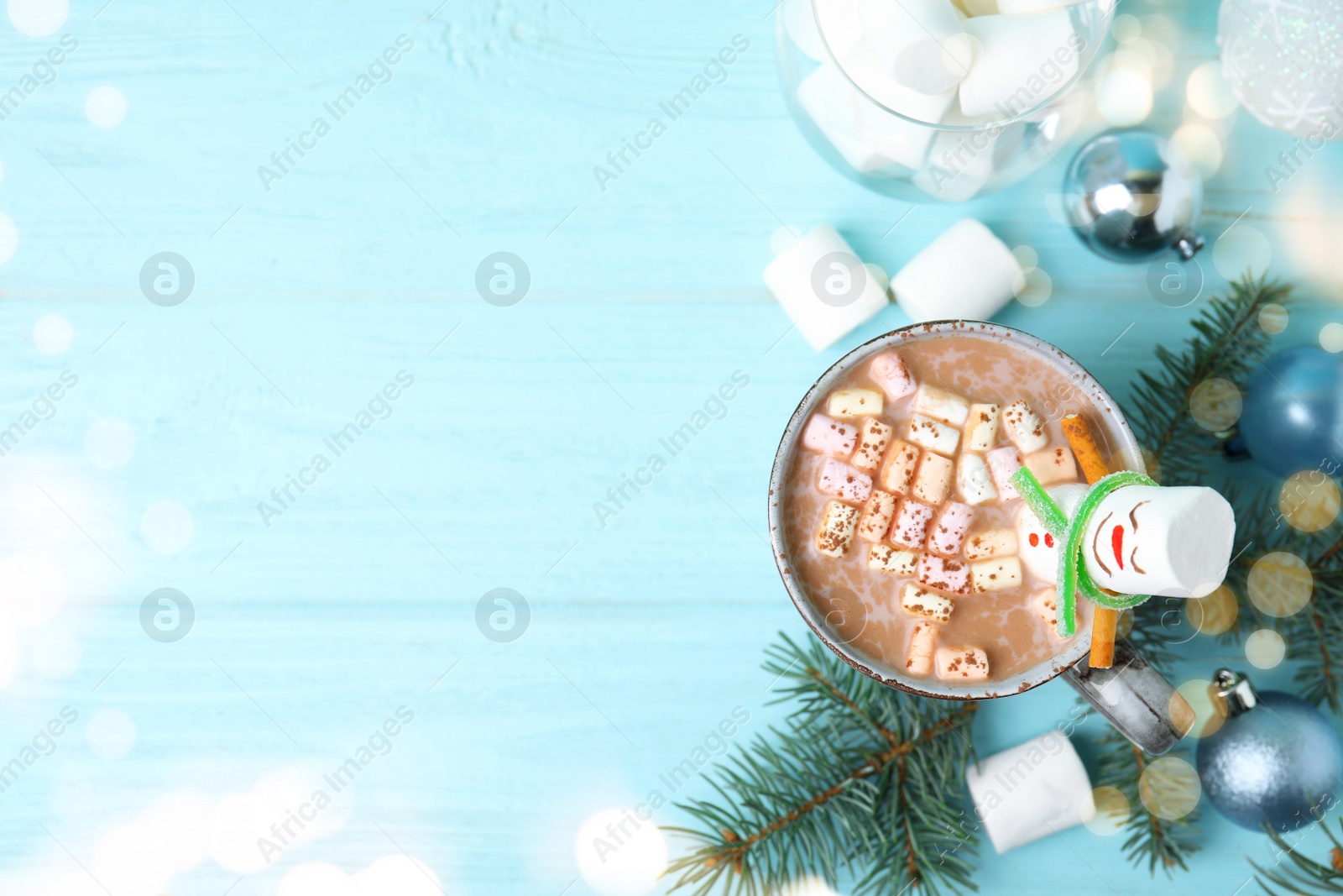 Image of Funny marshmallow snowman in cup of hot drink on light blue wooden table, flat lay. Space for text