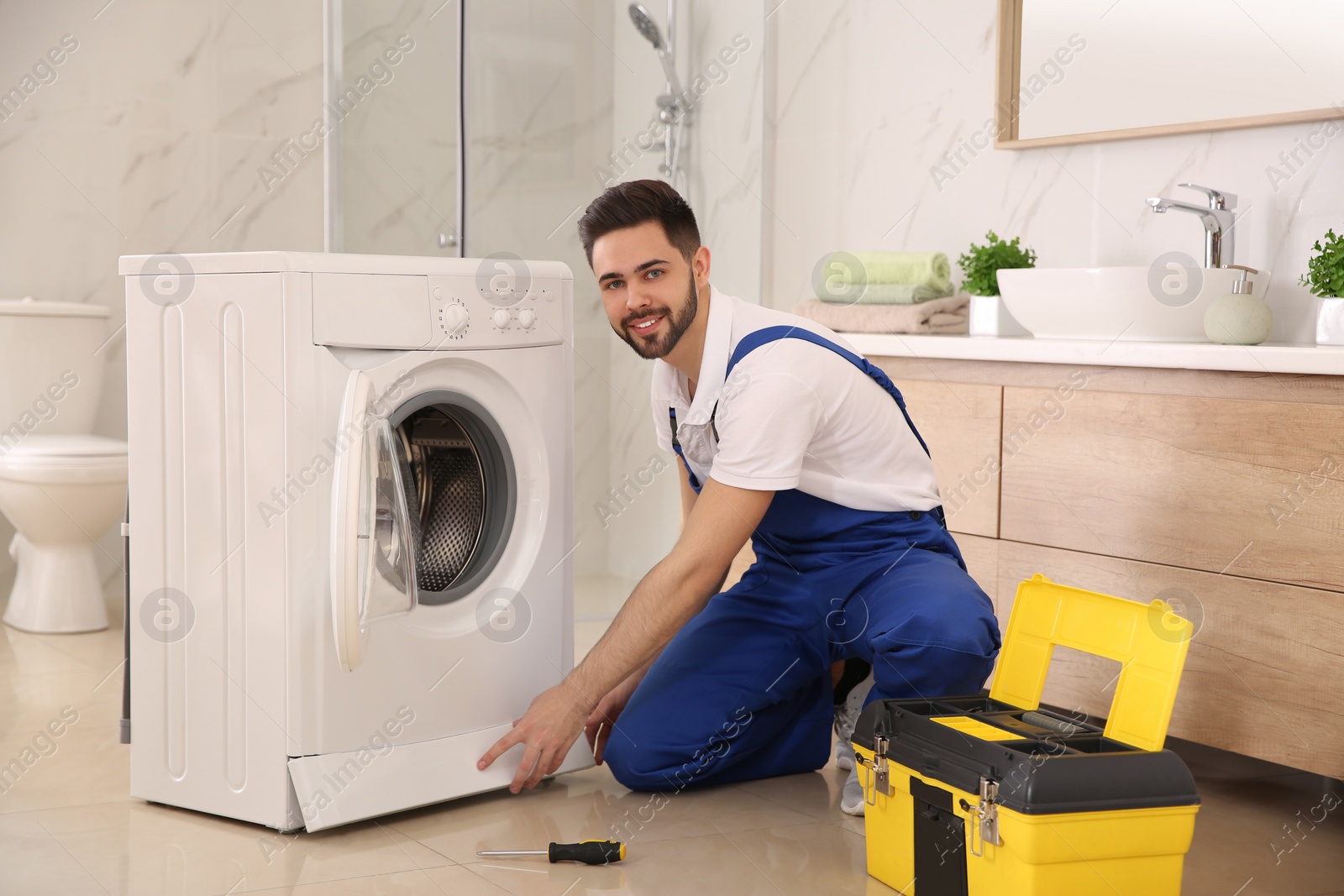 Photo of Professional plumber repairing washing machine in bathroom