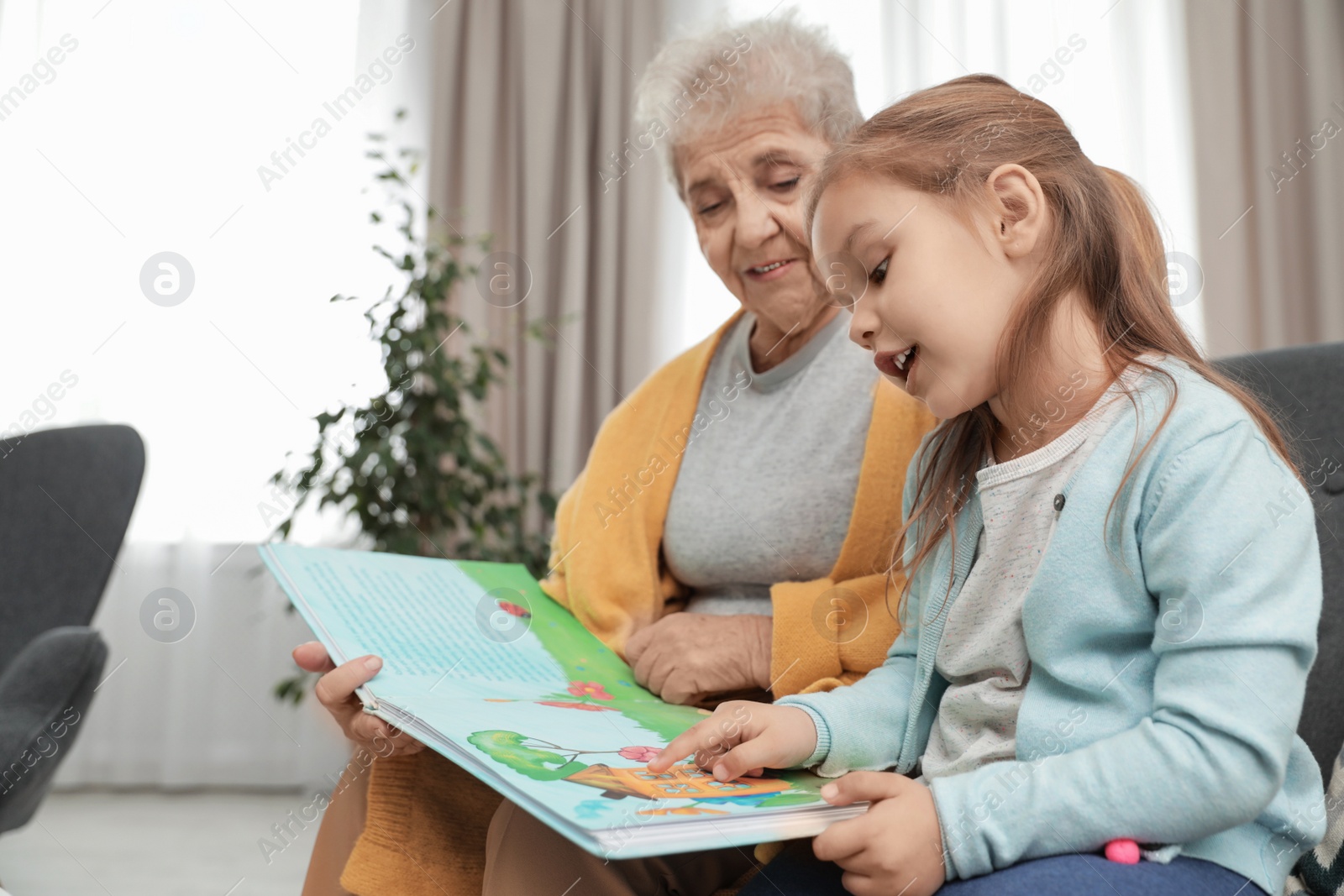 Photo of Cute girl and her grandmother reading book at home