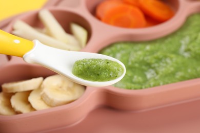 Photo of Healthy baby food. Spoon with delicious broccoli puree over section plate, closeup