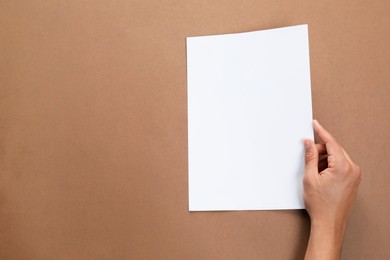 Man holding sheet of paper on brown background, closeup. Mockup for design