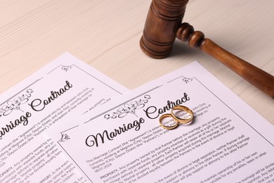 Photo of Marriage contracts, gold rings and gavel on light wooden table, closeup