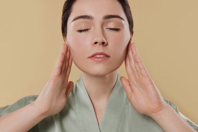 Photo of Young woman massaging her face on beige background