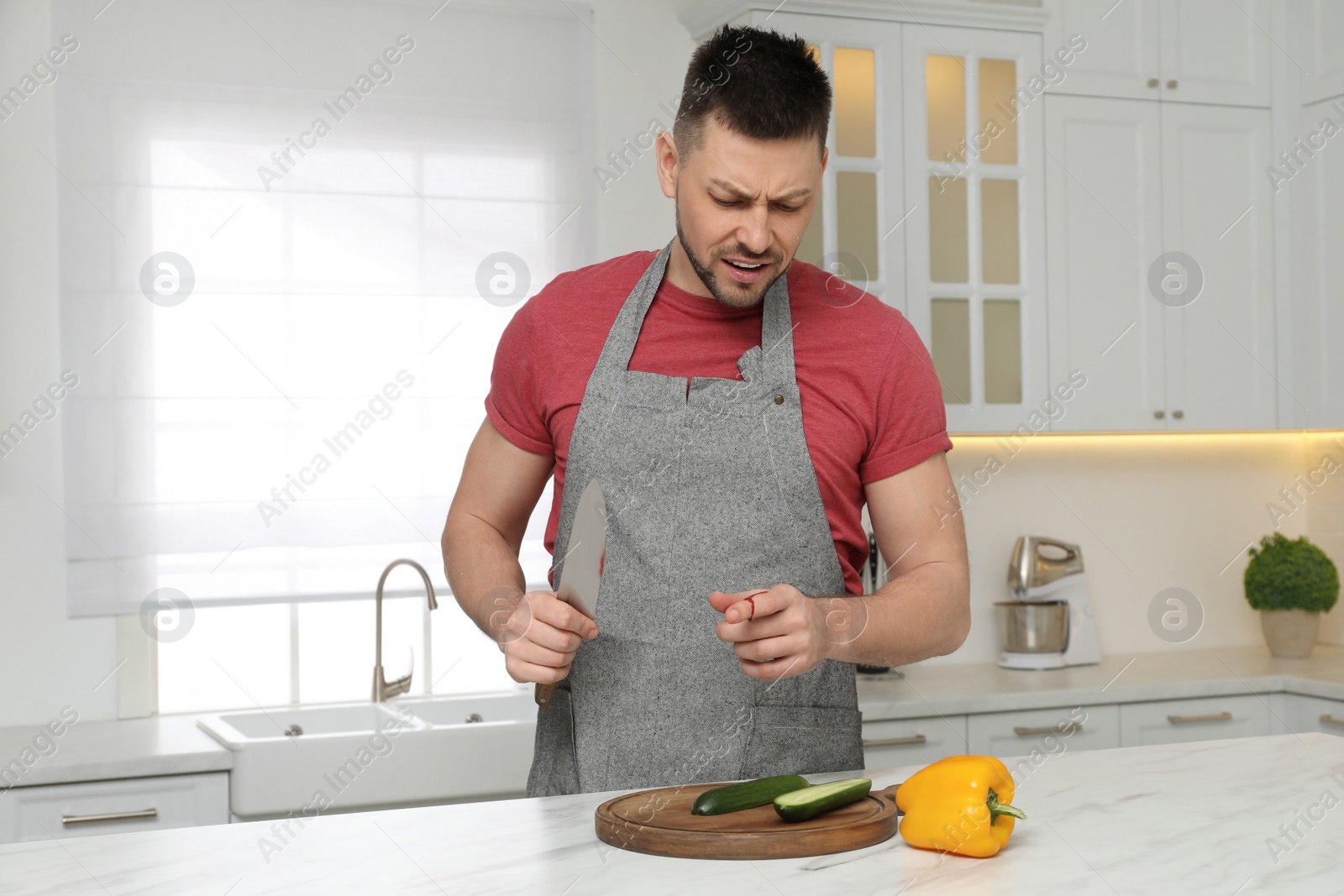 Photo of Man cut finger with knife while cooking at white marble table in kitchen