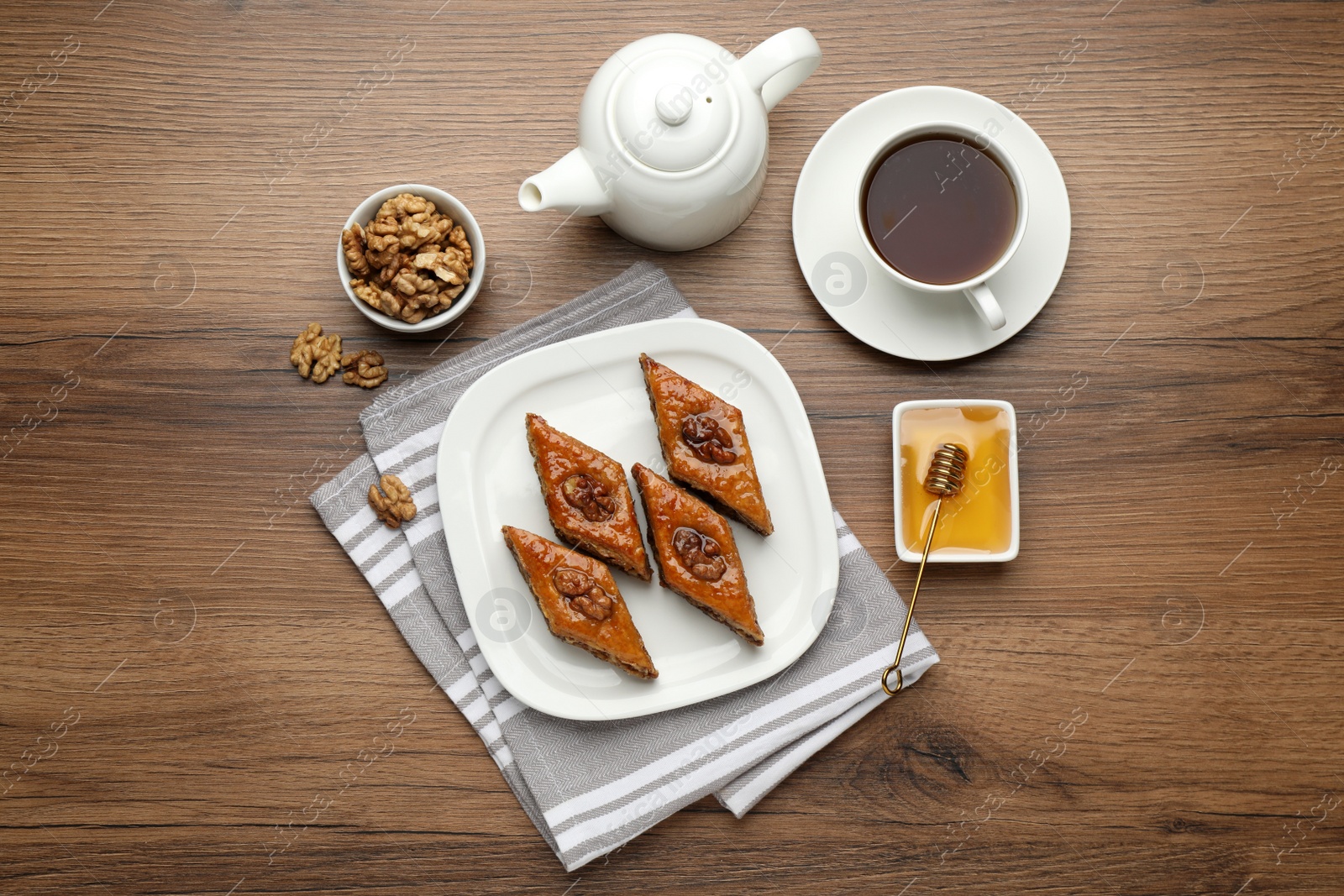 Photo of Delicious sweet baklava with walnuts, honey and hot tea on wooden table, flat lay