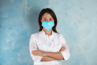 Photo of Doctor with disposable mask on face against light blue background