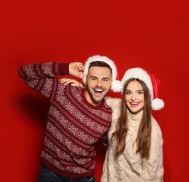 Photo of Couple wearing Christmas sweaters and Santa hats on red background