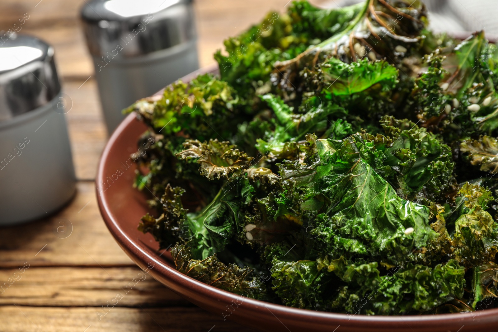 Photo of Tasty baked kale chips on wooden table, closeup