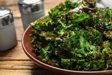 Tasty baked kale chips on wooden table, closeup