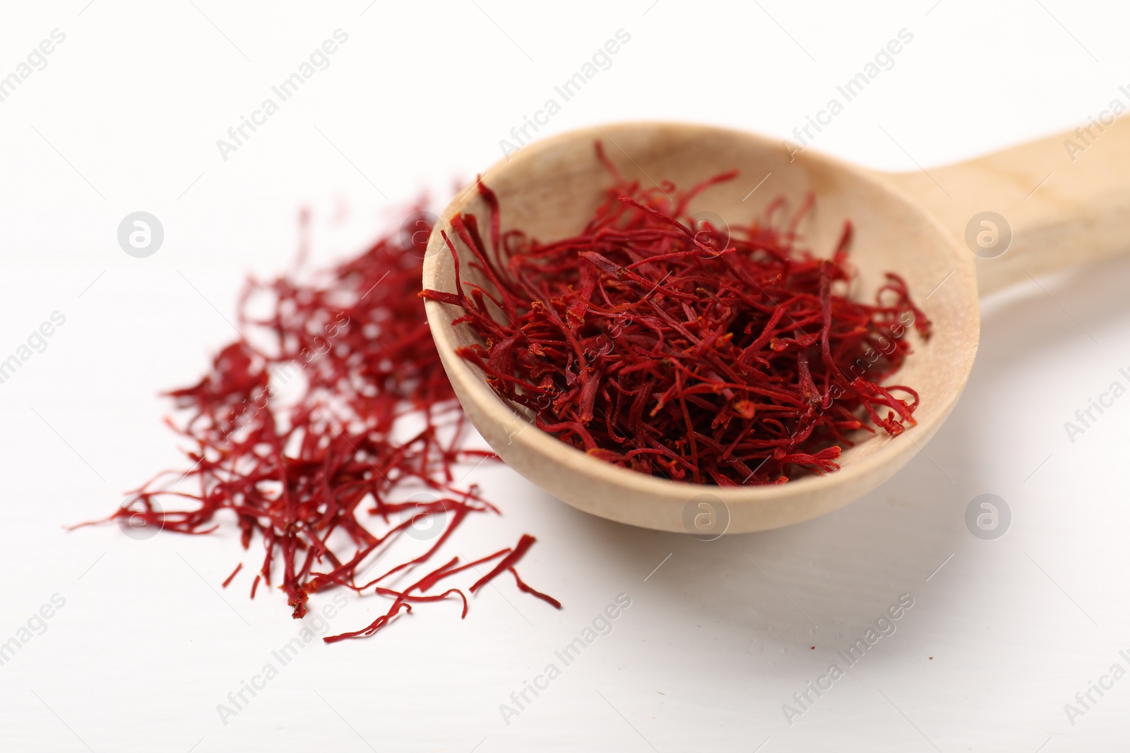 Photo of Aromatic saffron and spoon on white table, closeup