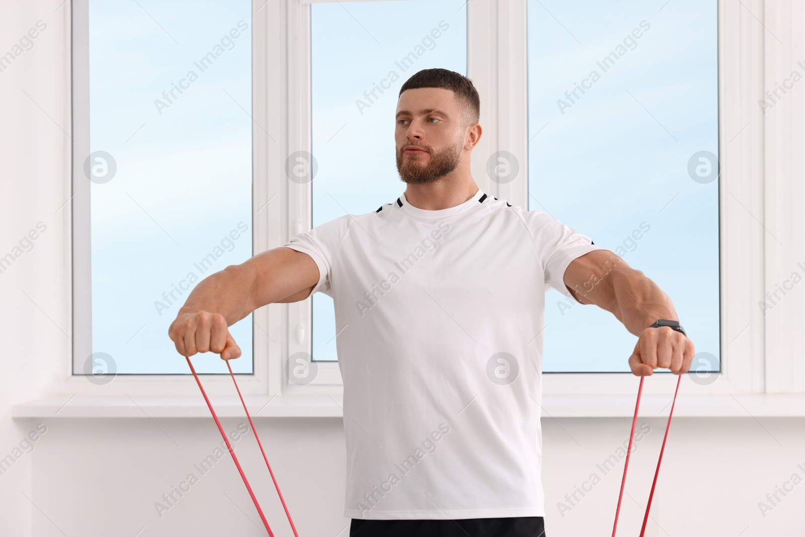 Photo of Athletic man doing exercise with elastic resistance band indoors