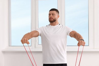 Athletic man doing exercise with elastic resistance band indoors