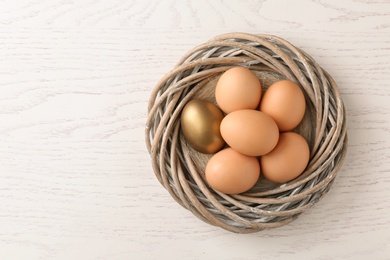 Photo of Golden egg among others in nest on wooden background, top view with space for text