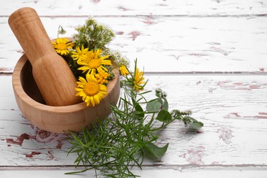 Mortar with pestle, flowers and herbs on white wooden table, space for text