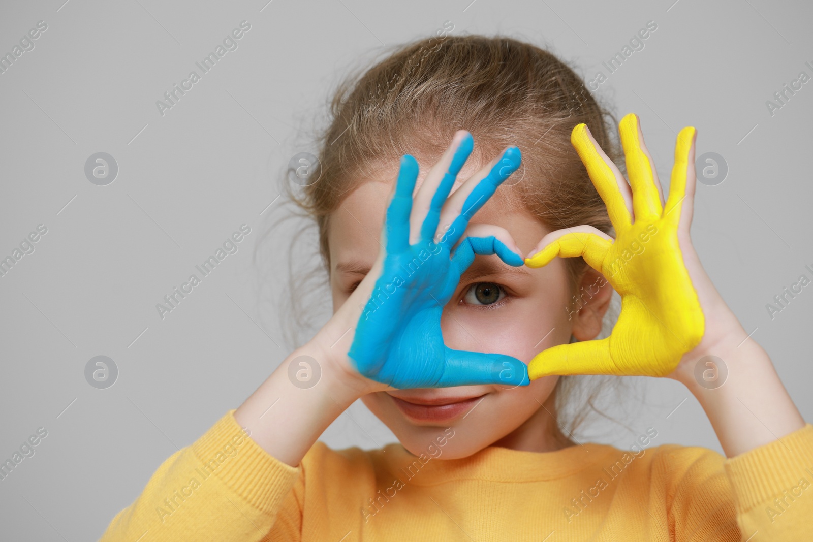 Photo of Little girl making heart with her hands painted in Ukrainian flag colors on light grey background, space for text. Love Ukraine concept