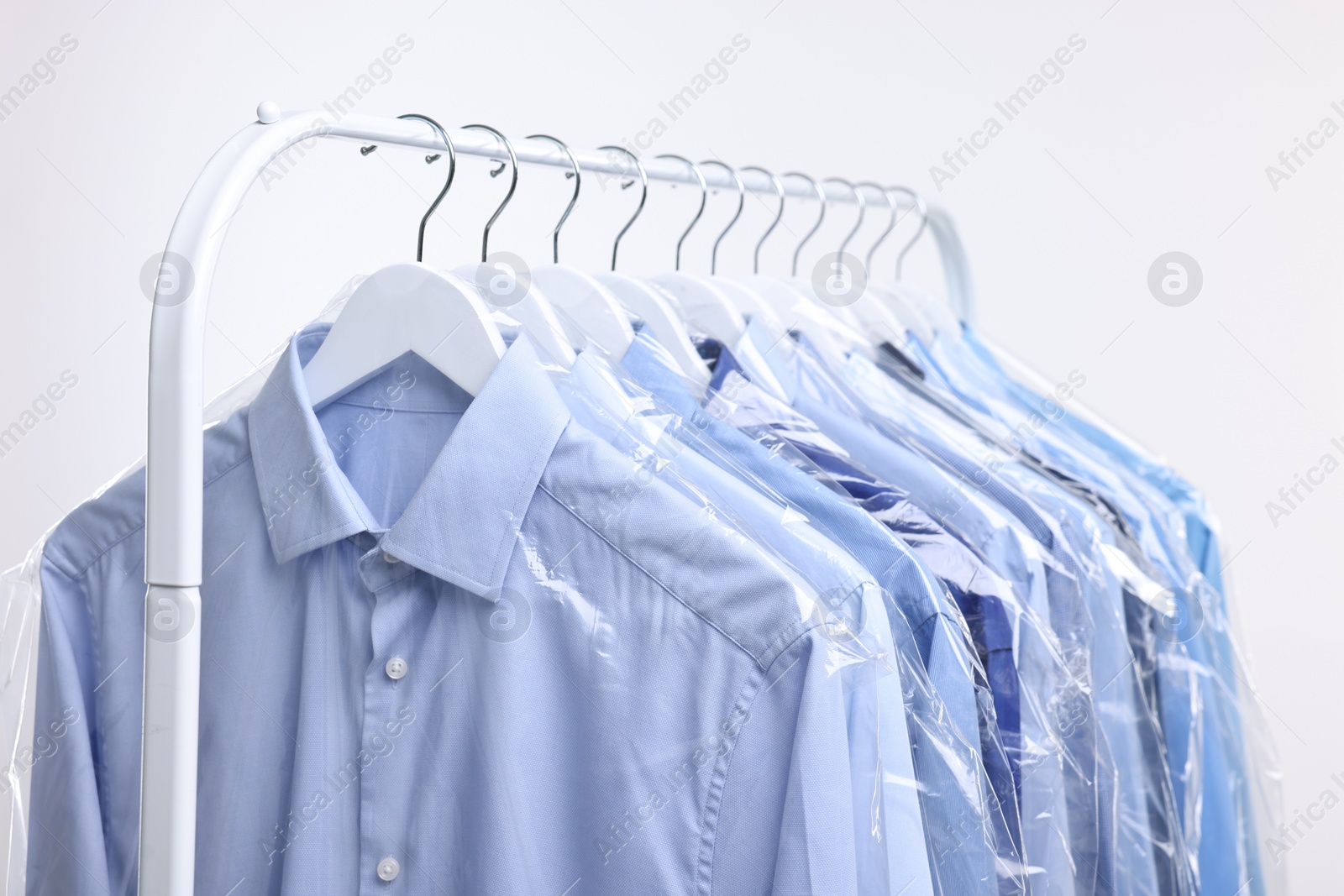 Photo of Dry-cleaning service. Many different clothes in plastic bags hanging on rack against white background, closeup