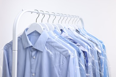 Photo of Dry-cleaning service. Many different clothes in plastic bags hanging on rack against white background, closeup