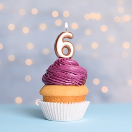Birthday cupcake with number six candle on table against festive lights