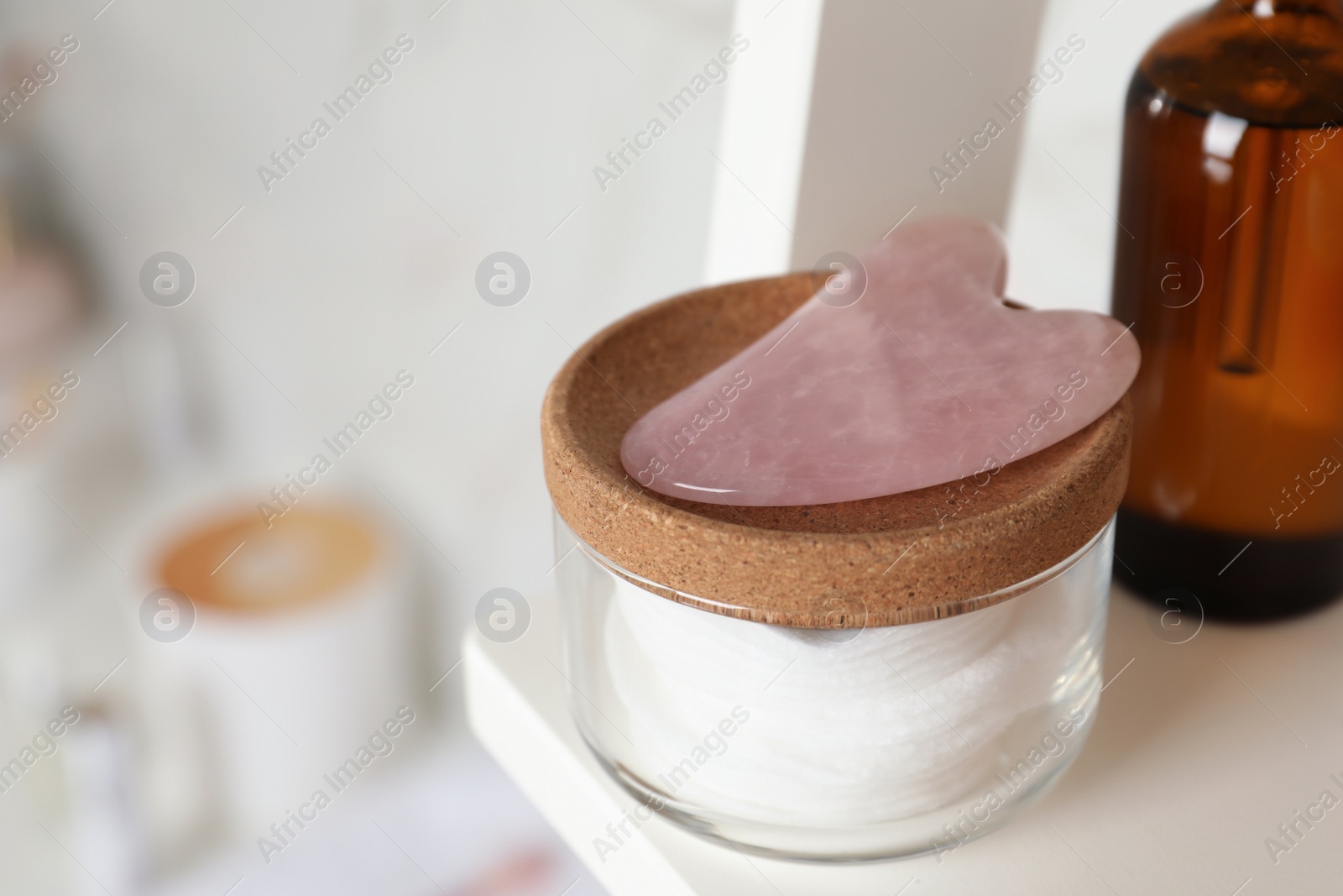 Photo of Rose quartz gua sha tool and toiletries on white shelf, closeup. Space for text