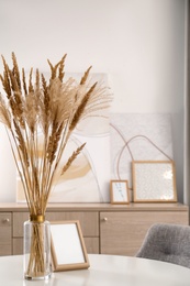 Photo of Dry plants and photoframe on white table indoors. Interior design
