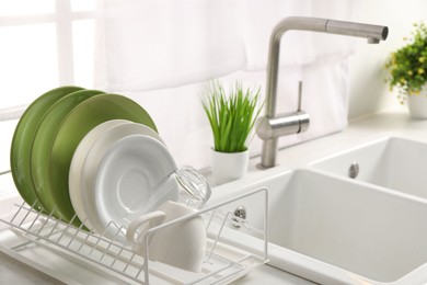 Drainer with different clean dishware, glass and cup on light table near sink indoors