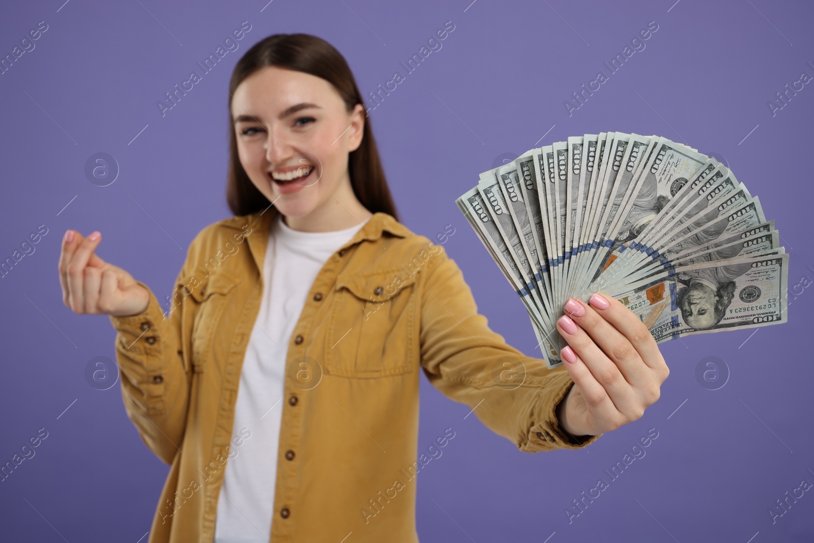 Photo of Happy woman with dollar banknotes showing money gesture on purple background, selective focus