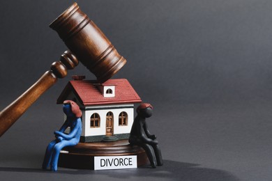 Photo of Word Divorce, house model, plasticine people figures and wooden gavel on dark background, space for text