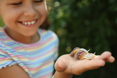 Photo of Girl playing with cute snails outdoors, focus on hand. Child spending time in nature
