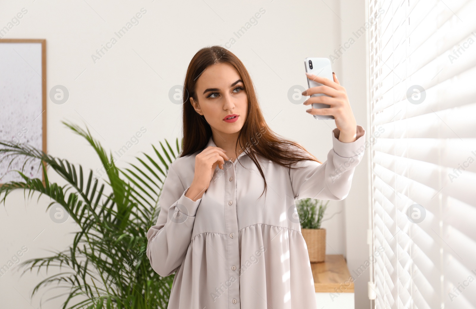 Photo of Beautiful woman taking selfie near window indoors