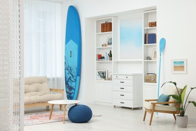 Photo of SUP board and modern furniture in stylish living room. Interior design
