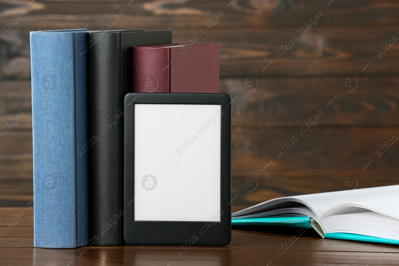 Photo of Portable e-book reader and many hardcover books on wooden table, space for text