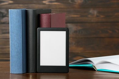 Photo of Portable e-book reader and many hardcover books on wooden table, space for text