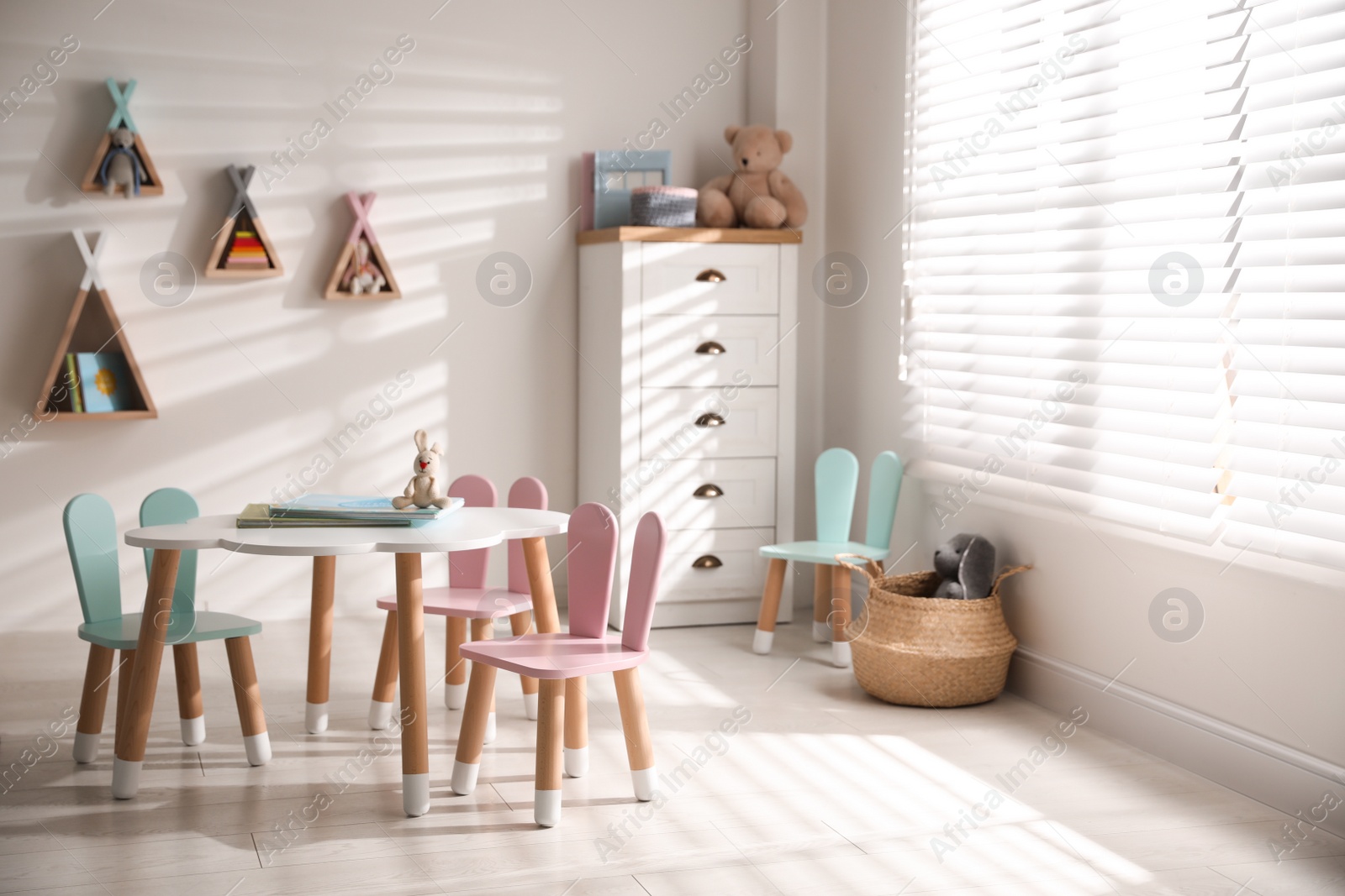 Photo of Small table and chairs with bunny ears in children's room interior