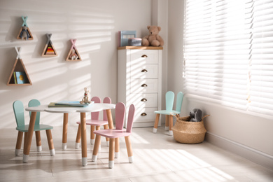 Photo of Small table and chairs with bunny ears in children's room interior