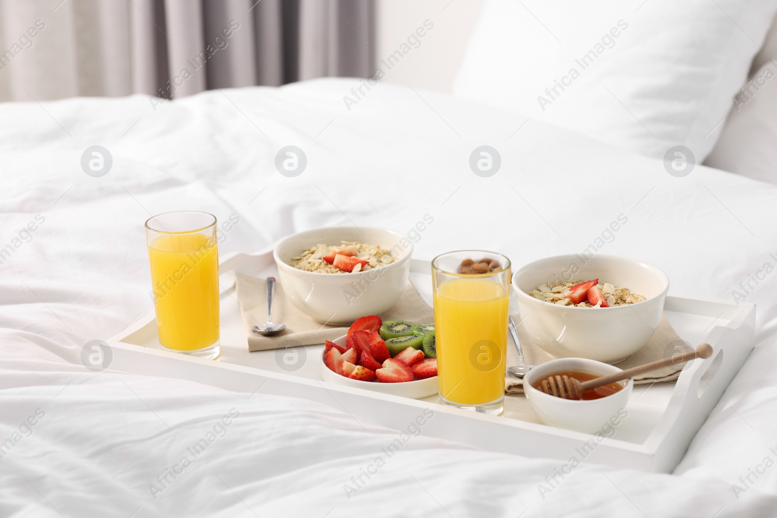 Tasty breakfast served in bed. Oatmeal, juice, fruits and honey on tray Photo of Tasty breakfast served in bed. Oatmeal, juice, fruits and honey on tray