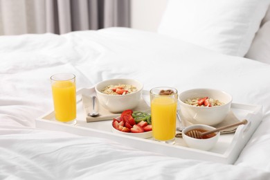 Photo of Tasty breakfast served in bed. Oatmeal, juice, fruits and honey on tray