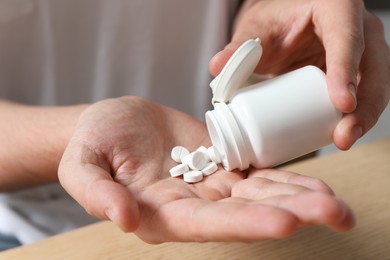 Photo of Man pouring pills from bottle at table, closeup