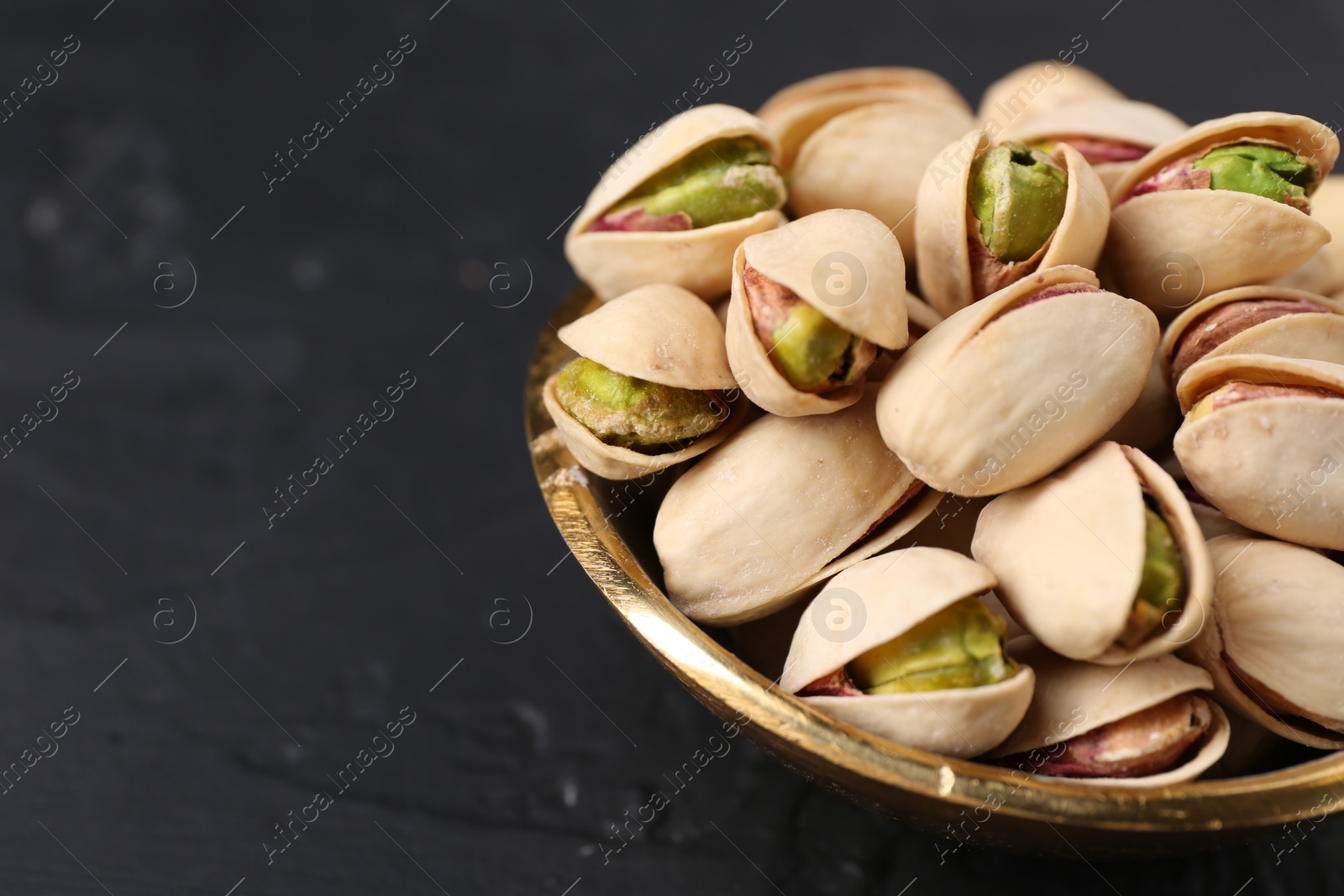 Photo of Tasty pistachios in bowl on black table, closeup. Space for text