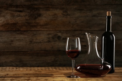 Photo of Decanter, glass and bottle with red wine on wooden table