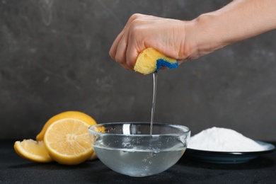 Photo of Woman squeezing out sponge over bowl with water and baking soda on dark table