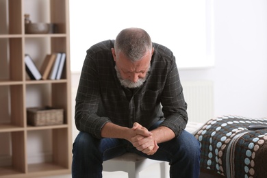 Photo of Depressed senior man sitting on stool indoors