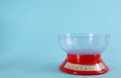 Kitchen scale with plastic bowl on light blue background, space for text